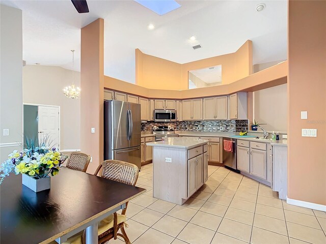 kitchen with light tile patterned floors, appliances with stainless steel finishes, backsplash, a kitchen island, and decorative light fixtures