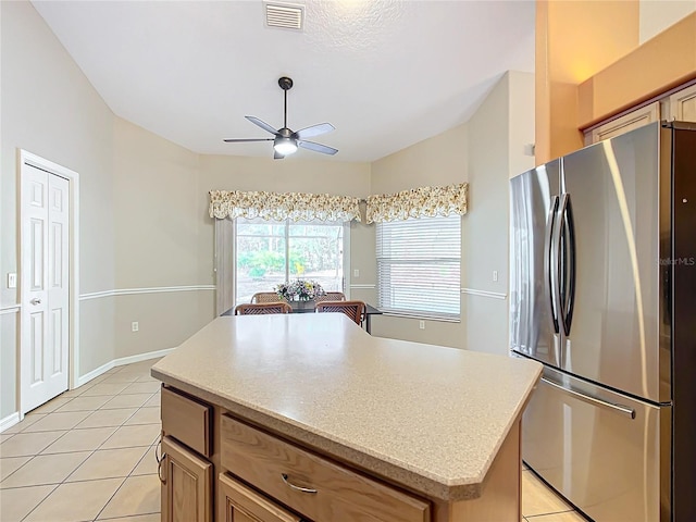 kitchen with light tile patterned flooring, a kitchen island, lofted ceiling, stainless steel fridge, and ceiling fan