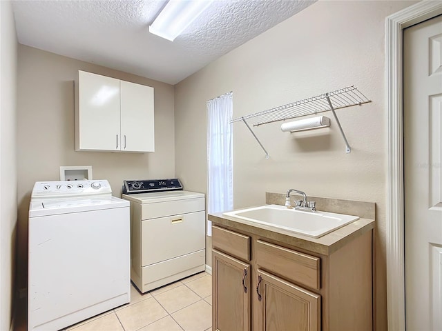 laundry room with sink, cabinets, light tile patterned floors, washing machine and clothes dryer, and a textured ceiling