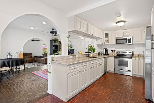 kitchen featuring sink, ceiling fan, stainless steel appliances, light stone counters, and white cabinets