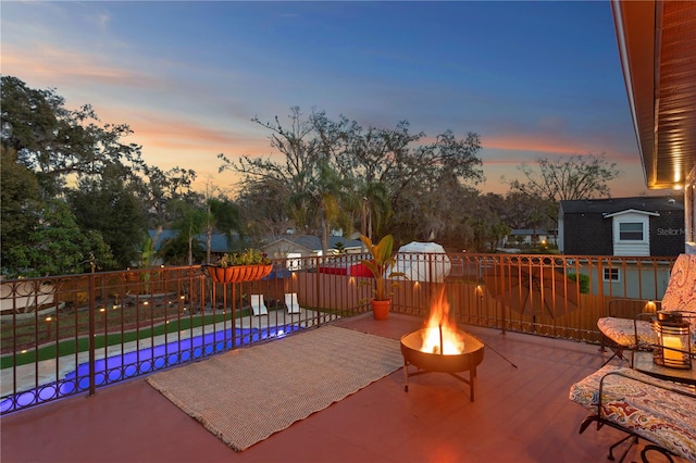 patio terrace at dusk with an outdoor fire pit and a fenced in pool