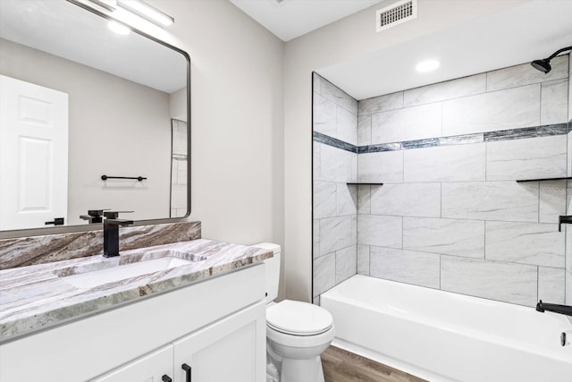 full bathroom with vanity, hardwood / wood-style floors, tiled shower / bath combo, and toilet