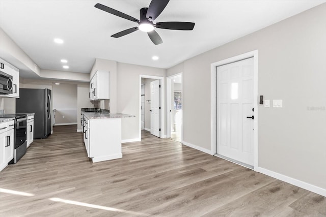 kitchen with stainless steel appliances, white cabinets, light hardwood / wood-style floors, and dark stone counters