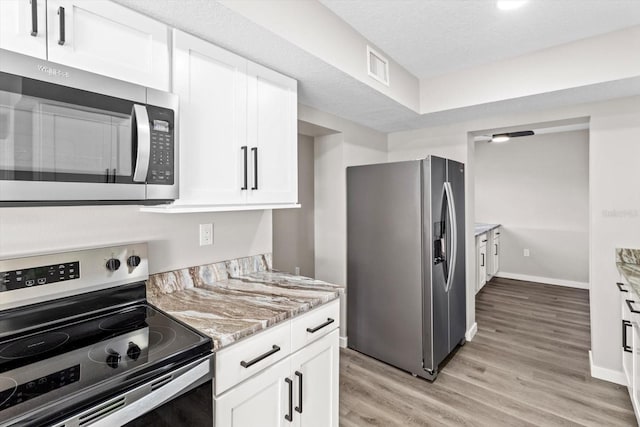 kitchen featuring light stone counters, a textured ceiling, stainless steel appliances, light hardwood / wood-style floors, and white cabinets