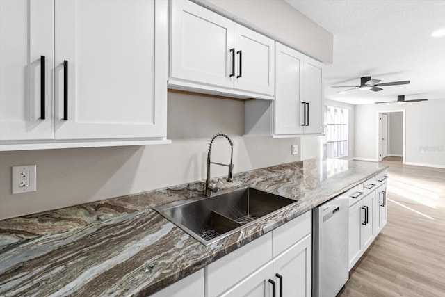 kitchen with sink, white cabinetry, dark stone countertops, stainless steel dishwasher, and light hardwood / wood-style floors