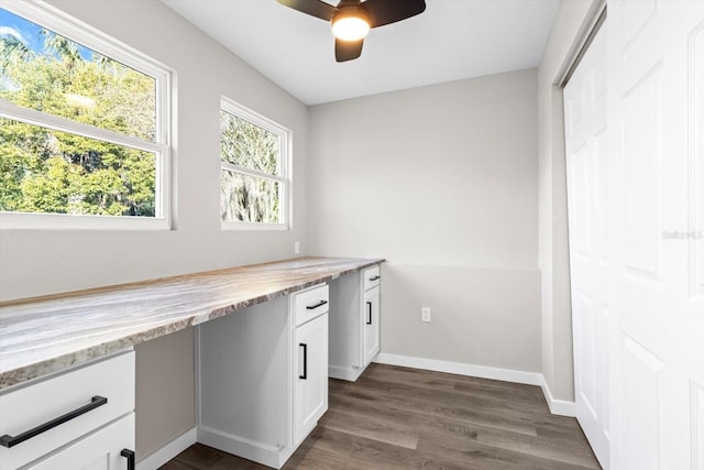 unfurnished office featuring dark wood-type flooring, built in desk, and ceiling fan