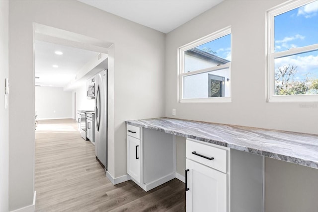 kitchen with light stone counters, a healthy amount of sunlight, light wood-type flooring, and white cabinets