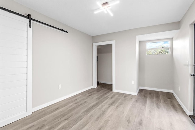 unfurnished bedroom featuring a barn door and light hardwood / wood-style flooring