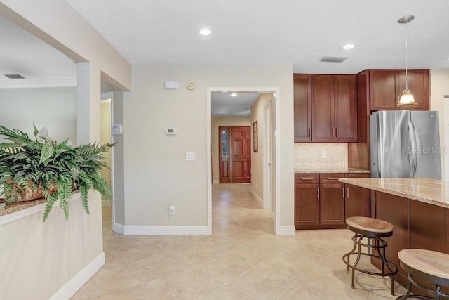 kitchen with a breakfast bar, tasteful backsplash, stainless steel fridge, hanging light fixtures, and light stone countertops