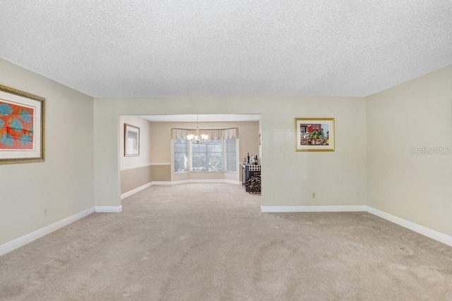 carpeted spare room with a textured ceiling and a chandelier