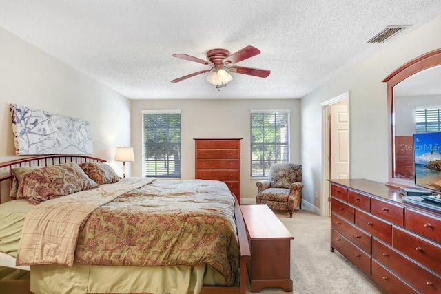 bedroom featuring ceiling fan, multiple windows, light carpet, and a textured ceiling