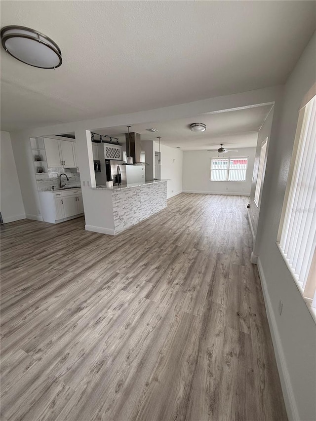 unfurnished living room featuring ceiling fan, sink, a textured ceiling, and light wood-type flooring