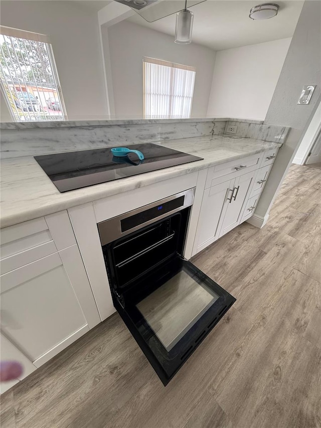 kitchen with light stone counters, black electric stovetop, light hardwood / wood-style floors, white cabinets, and oven