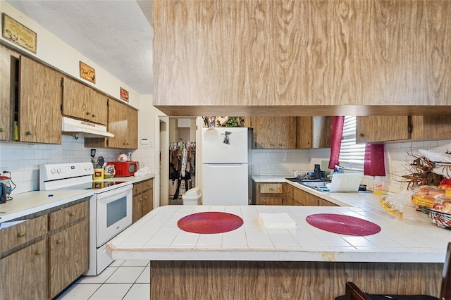 kitchen featuring light tile patterned flooring, tile counters, kitchen peninsula, white appliances, and backsplash