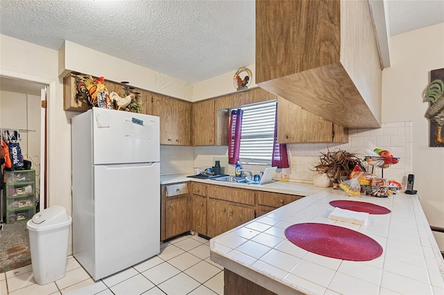 kitchen with decorative backsplash, tile countertops, sink, and white fridge