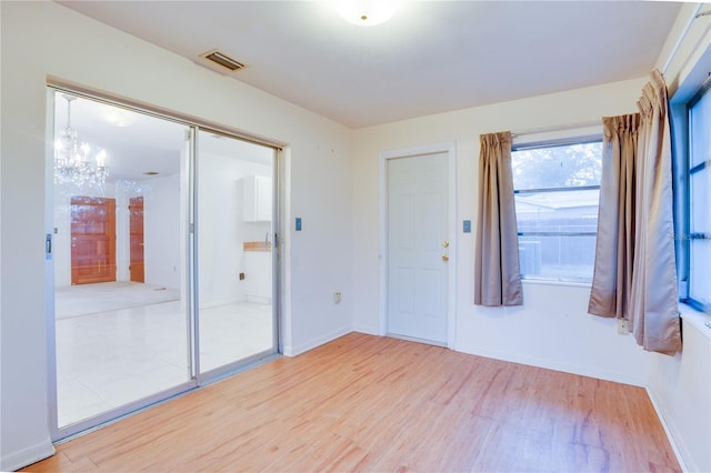 empty room with a notable chandelier and light hardwood / wood-style floors