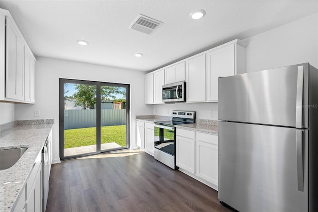 kitchen with appliances with stainless steel finishes, dark hardwood / wood-style flooring, light stone countertops, and white cabinets