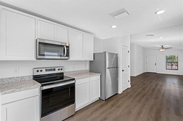 kitchen with appliances with stainless steel finishes, white cabinets, light stone counters, ceiling fan, and dark wood-type flooring