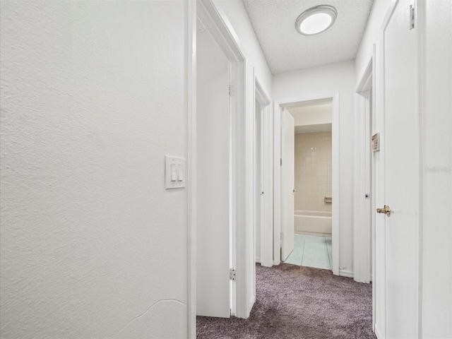 hall with dark carpet and a textured ceiling