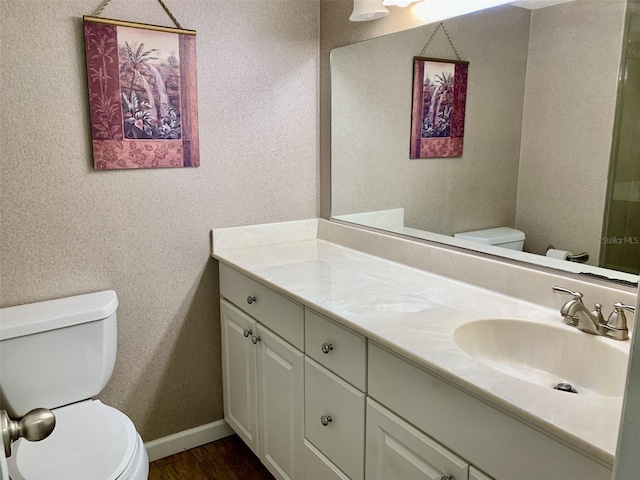 bathroom with baseboards, vanity, toilet, and wood finished floors