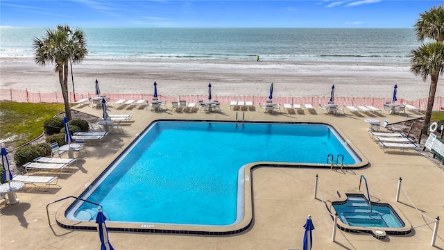 view of pool with a view of the beach, a community hot tub, a patio, and a water view