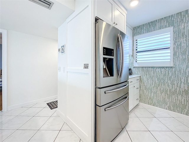 kitchen featuring light tile patterned floors, stainless steel fridge, and white cabinets