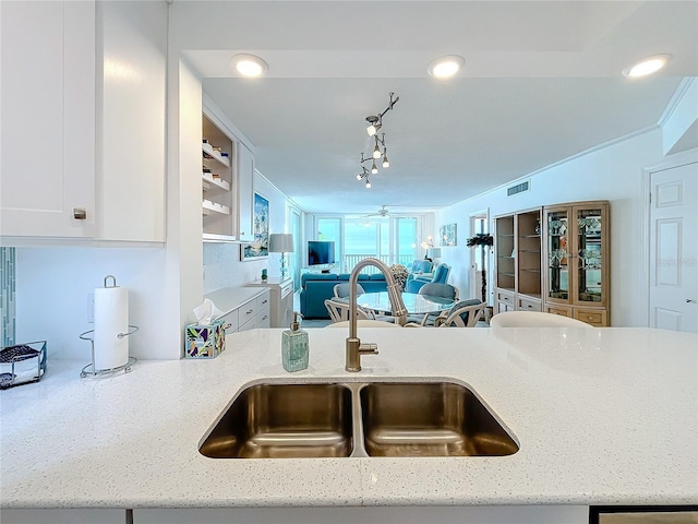 kitchen with track lighting, light stone countertops, sink, and white cabinets