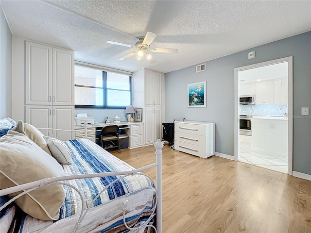 bedroom with a textured ceiling, ensuite bath, ceiling fan, and light wood-type flooring