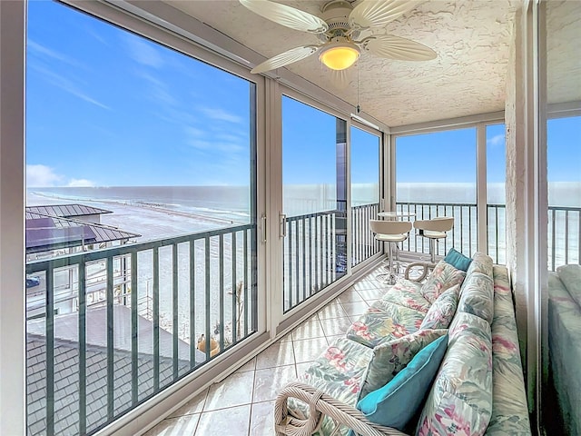 sunroom with a water view, ceiling fan, and a view of the beach