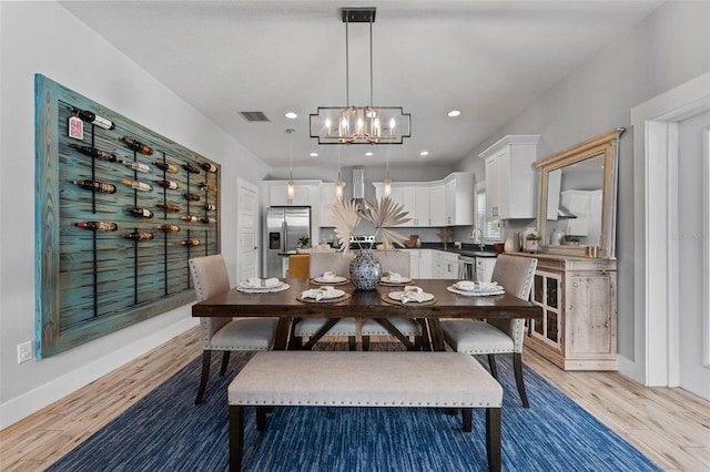 dining space with sink, a chandelier, and light wood-type flooring