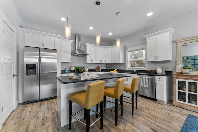 kitchen with pendant lighting, wall chimney range hood, stainless steel appliances, and white cabinets