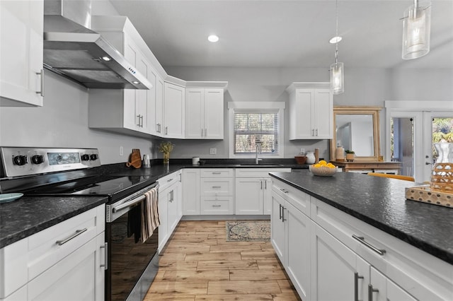 kitchen with stainless steel electric stove, white cabinetry, sink, hanging light fixtures, and wall chimney range hood