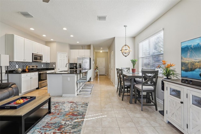 kitchen with a breakfast bar area, appliances with stainless steel finishes, white cabinets, a center island with sink, and decorative light fixtures