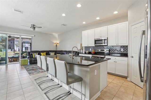 kitchen with sink, a breakfast bar area, appliances with stainless steel finishes, white cabinets, and a center island with sink