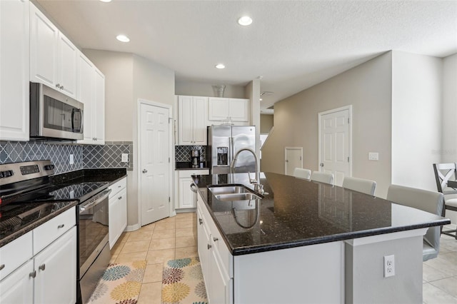 kitchen with appliances with stainless steel finishes, tasteful backsplash, white cabinetry, sink, and a center island with sink