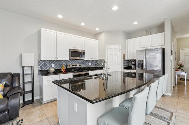 kitchen with stainless steel appliances, white cabinetry, a center island with sink, and dark stone counters