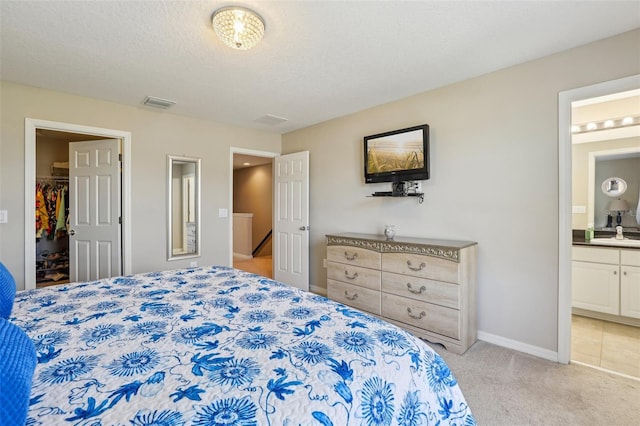 carpeted bedroom with sink, ensuite bath, a textured ceiling, and a spacious closet