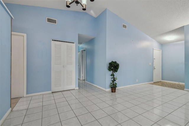 tiled spare room featuring a textured ceiling and high vaulted ceiling