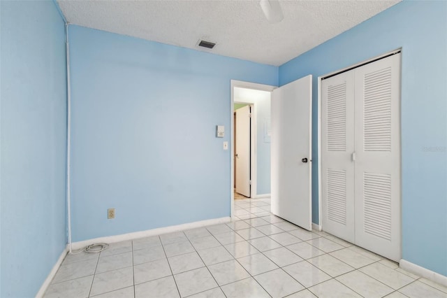 unfurnished bedroom featuring ceiling fan, light tile patterned floors, a textured ceiling, and a closet