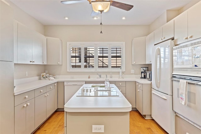 kitchen with white appliances, light hardwood / wood-style flooring, a kitchen island, ceiling fan, and white cabinets