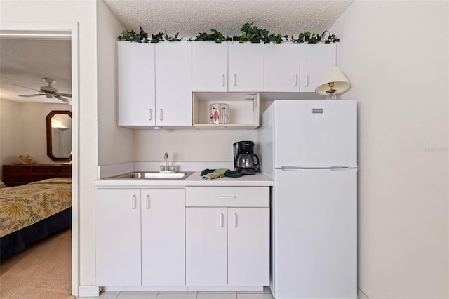 kitchen with white cabinetry, white fridge, sink, and a textured ceiling