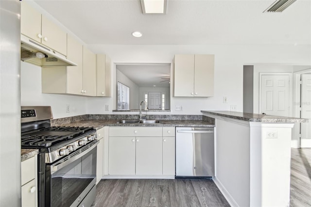 kitchen with sink, appliances with stainless steel finishes, cream cabinets, dark hardwood / wood-style flooring, and kitchen peninsula