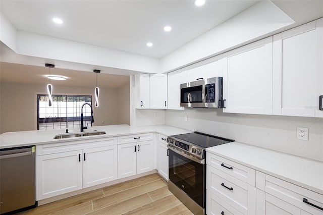 kitchen featuring pendant lighting, sink, appliances with stainless steel finishes, white cabinets, and kitchen peninsula