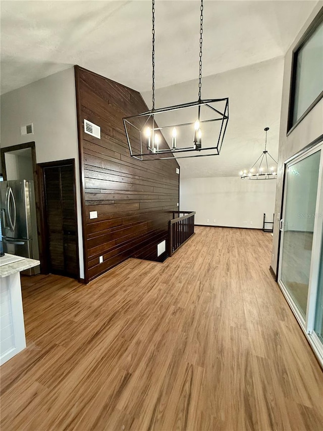 interior space featuring a high ceiling, light hardwood / wood-style floors, a chandelier, and wood walls