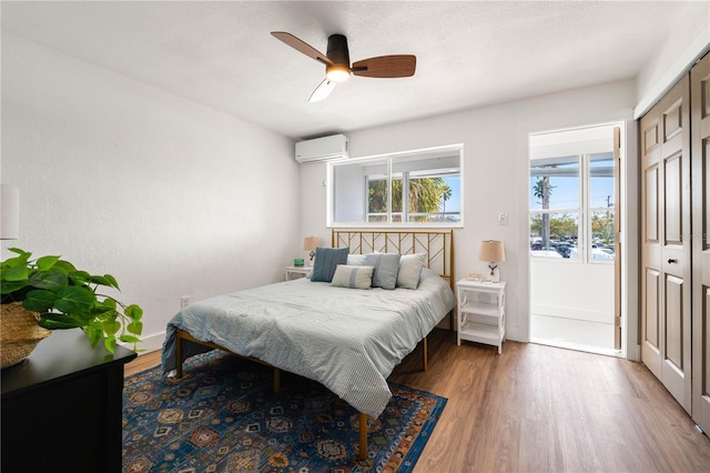 bedroom featuring hardwood / wood-style floors, a closet, an AC wall unit, and ceiling fan