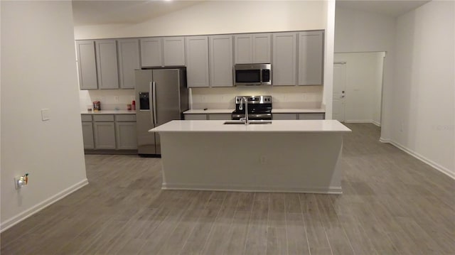 kitchen featuring stainless steel appliances, light hardwood / wood-style floors, vaulted ceiling, and gray cabinetry