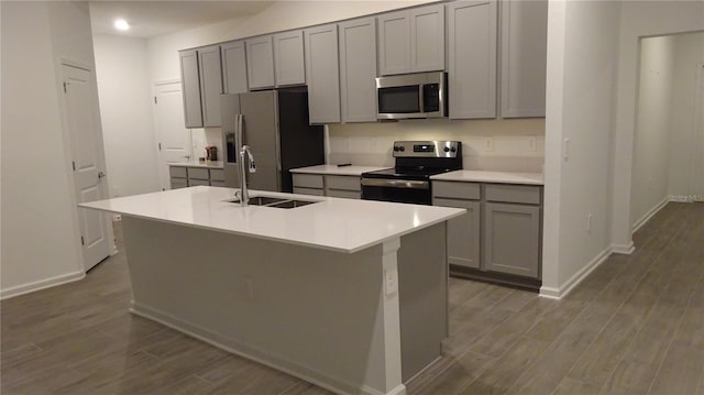 kitchen featuring gray cabinets, hardwood / wood-style floors, sink, a kitchen island with sink, and stainless steel appliances