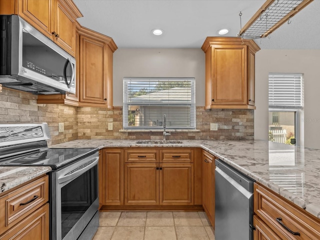 kitchen with appliances with stainless steel finishes, sink, decorative backsplash, light tile patterned floors, and light stone counters