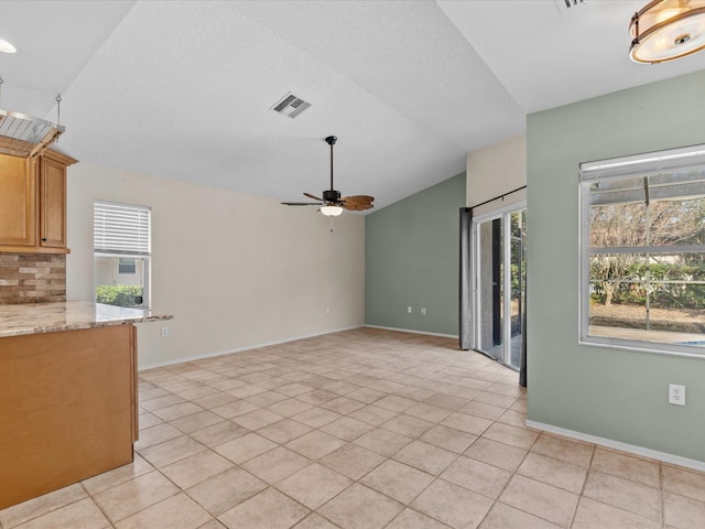 unfurnished living room with ceiling fan, light tile patterned floors, vaulted ceiling, and a wealth of natural light