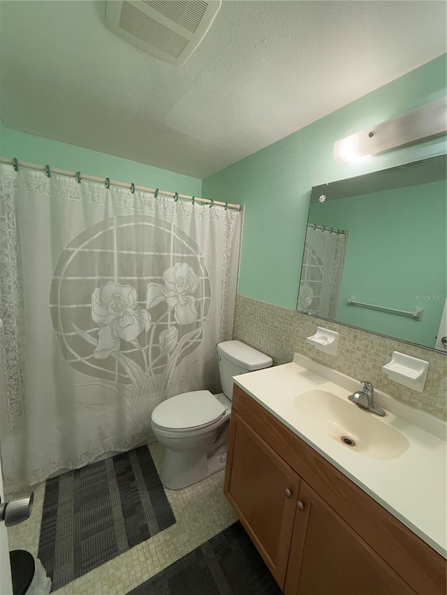 bathroom with toilet, a textured ceiling, tile walls, vanity, and tile patterned flooring